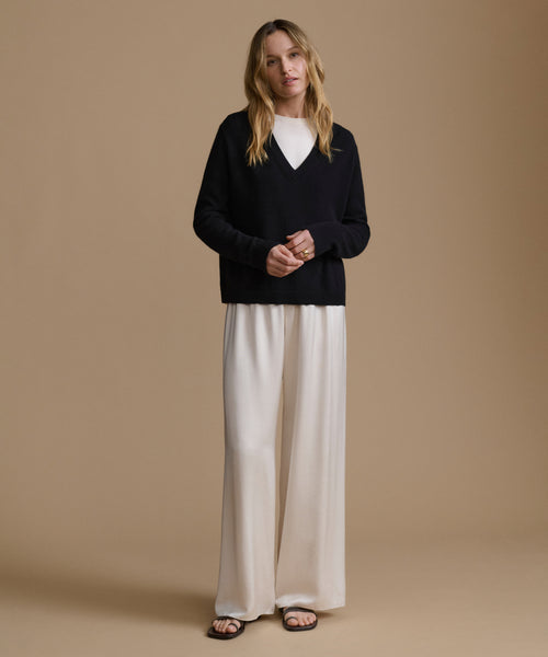 Woman wearing a black sweater and white pants against a beige background