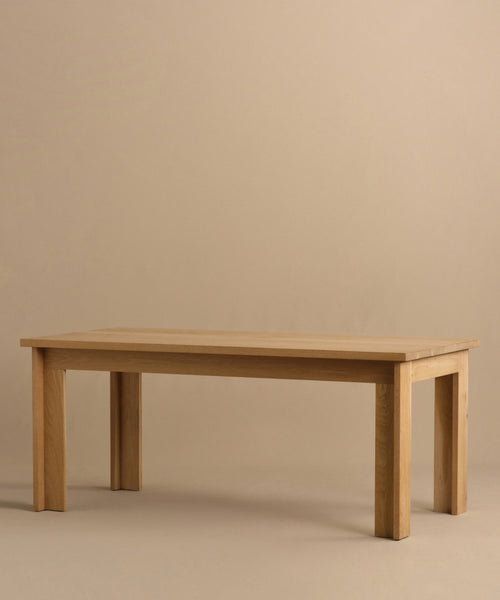 The Dining Table is a handmade rectangular piece crafted from solid white oak with four sturdy legs and is pictured against a plain beige background.