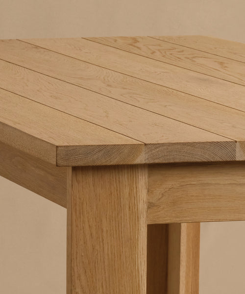 A close-up of the Dining Table, handmade from solid white oak with a natural finish. Its tabletop showcases visible grain and straight planks, supported by sturdy rectangular legs, set against a neutral beige background.