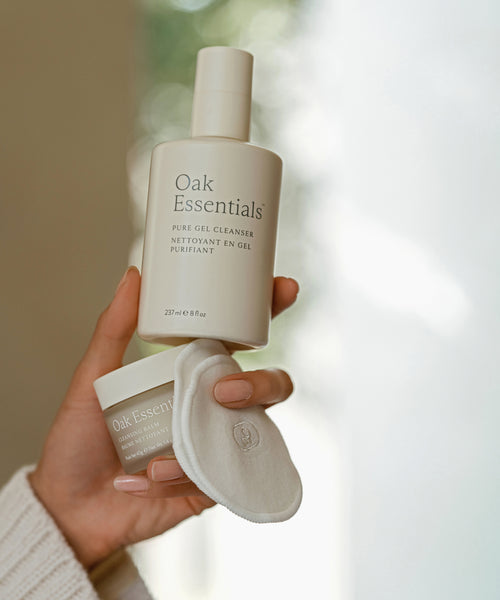 A hand holds the Double Cleanse Set and a round cotton pad against a soft, blurred background—perfect for achieving a hydrated complexion with this luxurious skincare ritual.