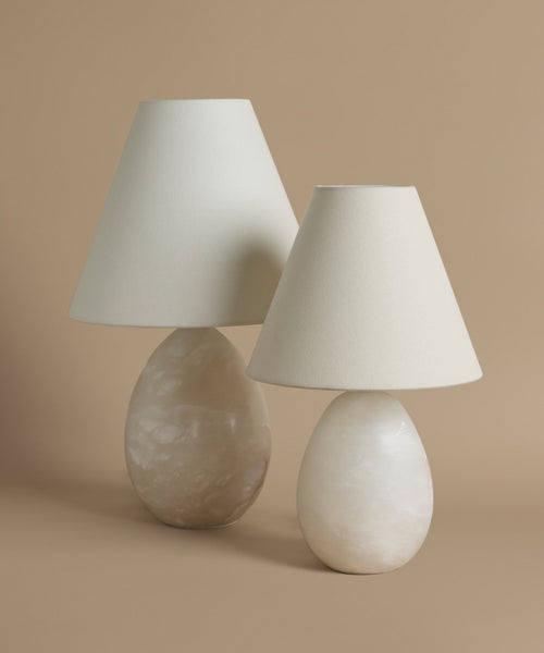 Two alabaster base, linen shade table lamps against a beige background.