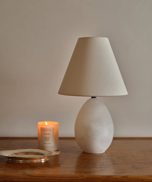 An alabaster base, linen shade table lamp on a wood table.