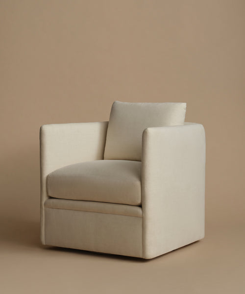 A modern square armchair upholstered in a warm cream-beige fabric, featuring a matching back cushion, set against a solid beige studio background.