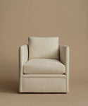 An upholstered accent chair in a warm cream or off-white fabric, featuring a square back cushion, wide armrests set against a solid beige studio background.