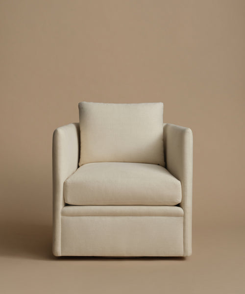 An upholstered accent chair in a warm cream or off-white fabric, featuring a square back cushion, wide armrests set against a solid beige studio background.
