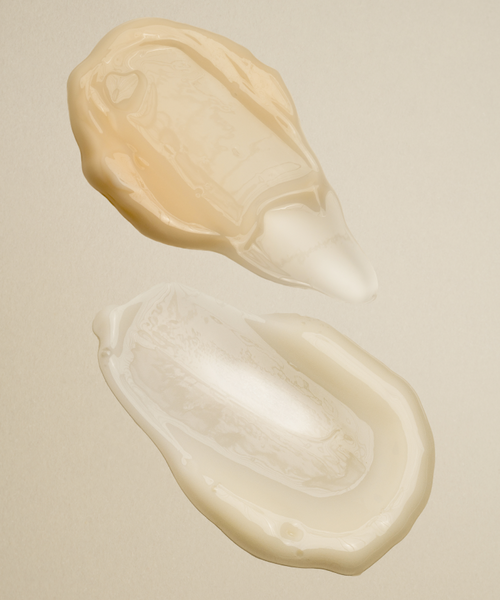Two blobs of Youthful Skin Serum Duo—one warm beige, the other clear with an off-white hue—are spread on a neutral background, each expertly formulated to boost hydration and support skin renewal.