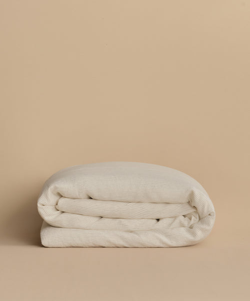 The Dusk Linen Duvet Cover is a lightweight, off-white linen cover featuring a subtle textured pattern, displayed against a plain beige background.
