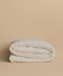 The Dusk Linen Duvet Cover, elegantly folded, rests on a plain beige surface with a matching beige background.