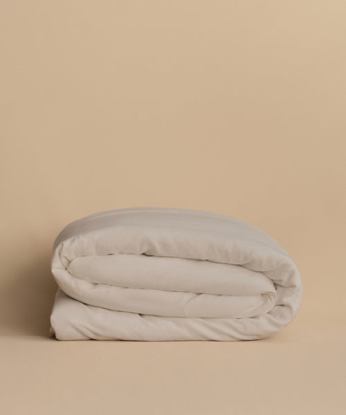 The Dusk Linen Duvet Cover, paired with a neatly folded white comforter, rests on a light beige surface against a matching beige background.