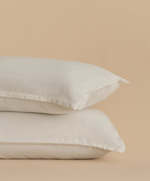Two Dusk Linen Pillow Shams in crisp white are stacked together, creating an inviting touch of luxury against a plain beige background—perfect for adding elegance to any space. Set includes 2 shams.
