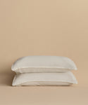 Two white pillows stacked together against a beige background, each featuring a Dusk Linen Pillow Sham Set of 2, adding a touch of luxury to the bedding.