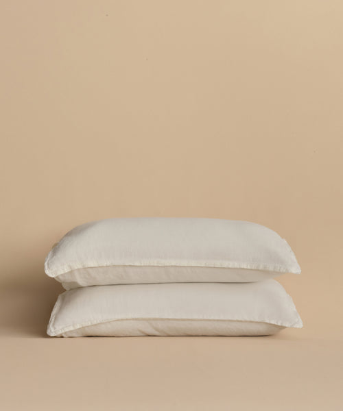 Two white pillows stacked together against a beige background, each featuring a Dusk Linen Pillow Sham Set of 2, adding a touch of luxury to the bedding.