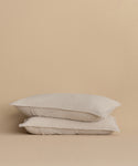 Two Dusk Linen Pillow Shams in light beige, made in Portugal, are stacked together against a plain beige background, highlighting their minimalist and neutral design.