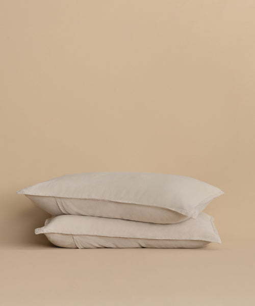 Two Dusk Linen Pillow Shams in light beige, made in Portugal, are stacked together against a plain beige background, highlighting their minimalist and neutral design.