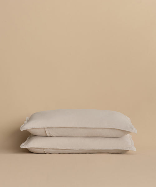 Two Dusk Linen Pillow Shams, in light beige and crafted from lightweight linen, are stacked neatly against a matching beige background.
