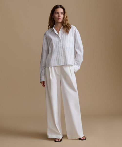 Woman wearing a blue and white stripe shirt with white pants against a beige background.