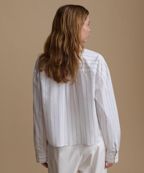 Woman wearing a blue and white stripe shirt with white pants against a beige background.