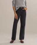A person wears the Easy Straight Crop luxury jeans in a straight cropped leg and mid-rise fit, paired with a light gray sweater, brown belt, and brown shoes, standing with one hand in their pocket against a plain background.