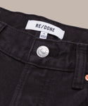 Close-up of the black denim Easy Straight Crop jeans’ waistband, featuring a silver button, belt loops, and a white RE/DONE label with size and origin details.