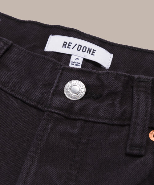 Close-up of the black denim Easy Straight Crop jeans’ waistband, featuring a silver button, belt loops, and a white RE/DONE label with size and origin details.