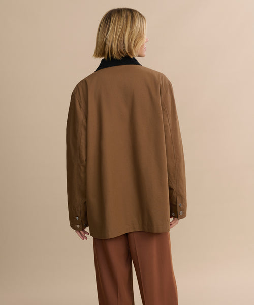 A person with shoulder-length blonde hair, wearing the Eaton Jacket and matching pants in brown, stands with their back to the camera against a plain beige background.