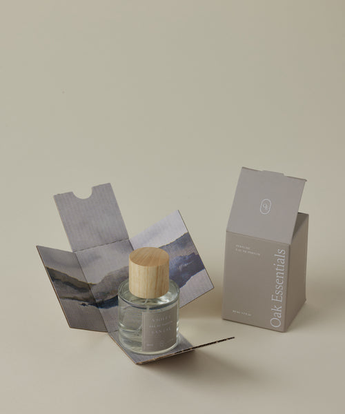 A glass jar with a wooden lid rests in an open decorative box beside a closed box labeled Violet Santal Eau De Parfum, evoking its clean scent and notes of wood and floral on a neutral background.