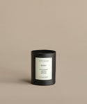 A black Ember Glass Candle with a white “jenni kayne Ember” label rests on a beige background. Hand-poured in Los Angeles, this natural candle features scent notes of black raspberry, plum, patchouli, birchwood, and birch.