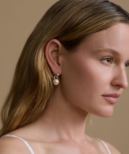 Close-up of a woman wearing a pearl earring against a beige background
