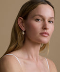Woman wearing pearl earrings against a beige background