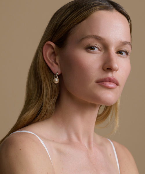 Woman wearing pearl earrings against a beige background