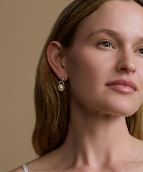 Close-up of a woman wearing pearl earrings against a beige background
