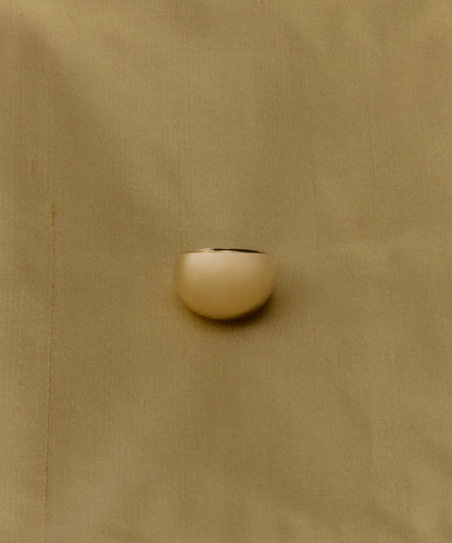 The Felix Dome Ring, featuring a smooth gold dome design, is displayed on a softly textured light tan fabric background.