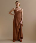 A woman with short blonde hair models the Florence Slip Dress, featuring thin straps and a fitted bodice in brown crepe, posing with one hand on her hip against a plain beige background.
