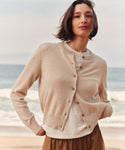 Woman wearing a oatmeal cashmere cardigan at the beach with a white t-shirt and brown pants.