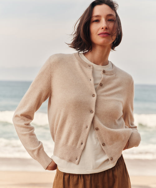 Woman wearing a oatmeal cashmere cardigan at the beach with a white t-shirt and brown pants.