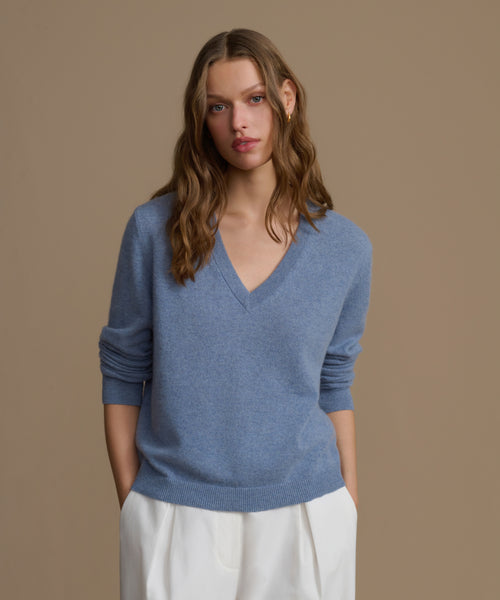 Woman wearing a blue cashmere sweater and white pants against a brown background