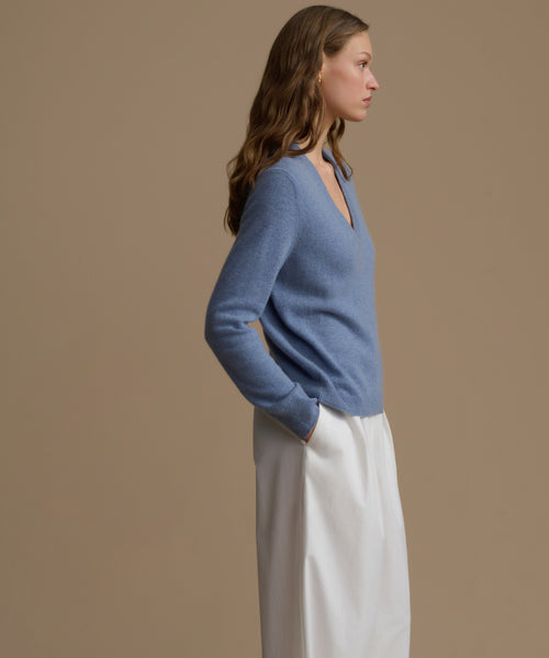 Woman wearing a blue cashmere sweater and white pants against a brown background