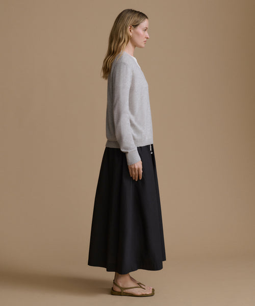 Woman wearing a light gray sweater and black skirt on a beige background