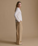 Woman wearing a white sweater and beige pants against a brown background
