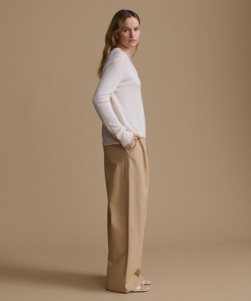 Woman wearing a white sweater and beige pants against a brown background