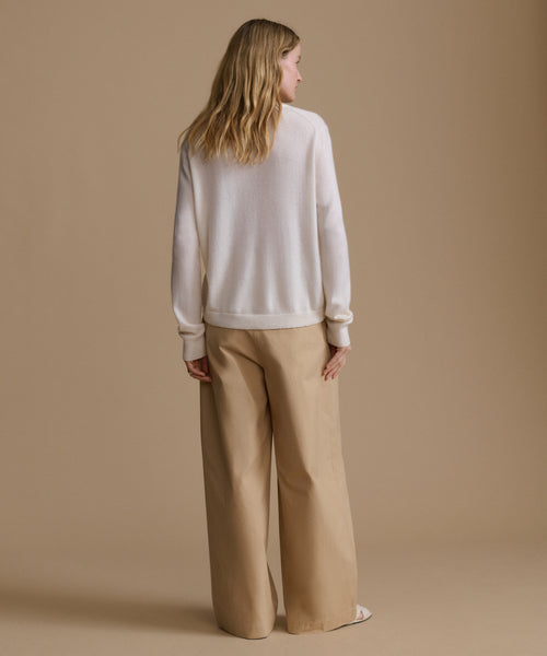 Woman wearing a white sweater and beige pants against a brown background