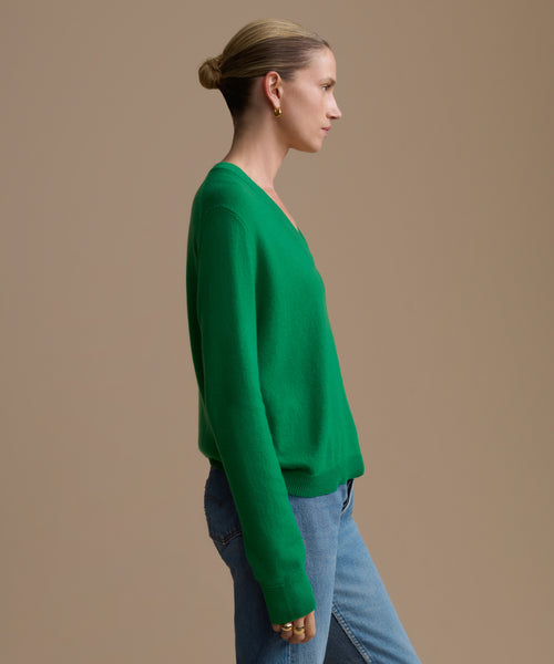 Woman wearing a green sweater and blue jeans against a beige background