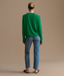 Person wearing a green sweater and blue jeans on a beige background