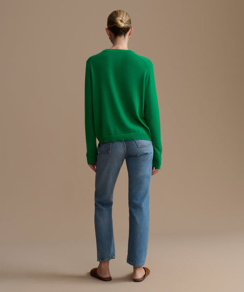 Person wearing a green sweater and blue jeans on a beige background
