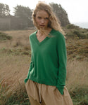 Woman wearing a green sweater and beige pants standing in a field.