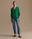 Person wearing a green sweater and blue jeans against a beige background