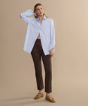 Woman wearing a light blue shirt and brown pants on a beige background