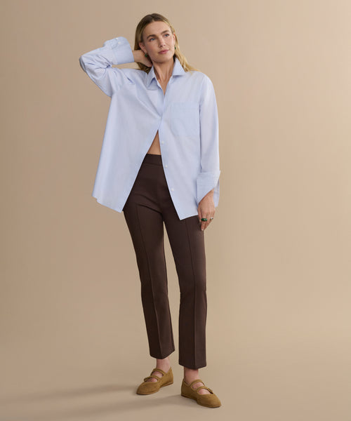Woman wearing a light blue shirt and brown pants on a beige background