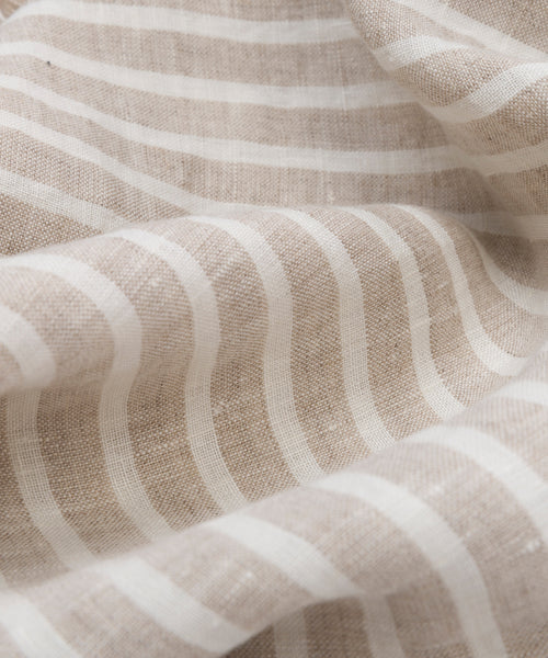 Close-up of the Frayed Linen Tablecloth, featuring white natural stripes, a soft textured weave, gentle folds, and subtle frayed edges.