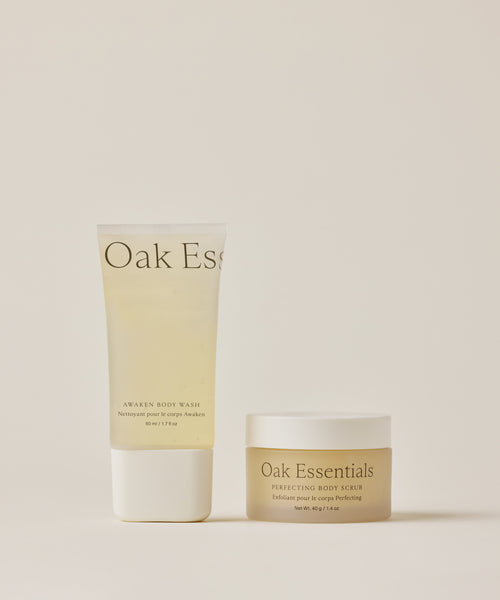 The Travel Fresh Start Set features two Oak Essentials products on a light beige background: a TSA-approved Awaken Body Wash and a small jar of Perfecting Body Scrub, both in minimal, elegant packaging—ideal for travel.